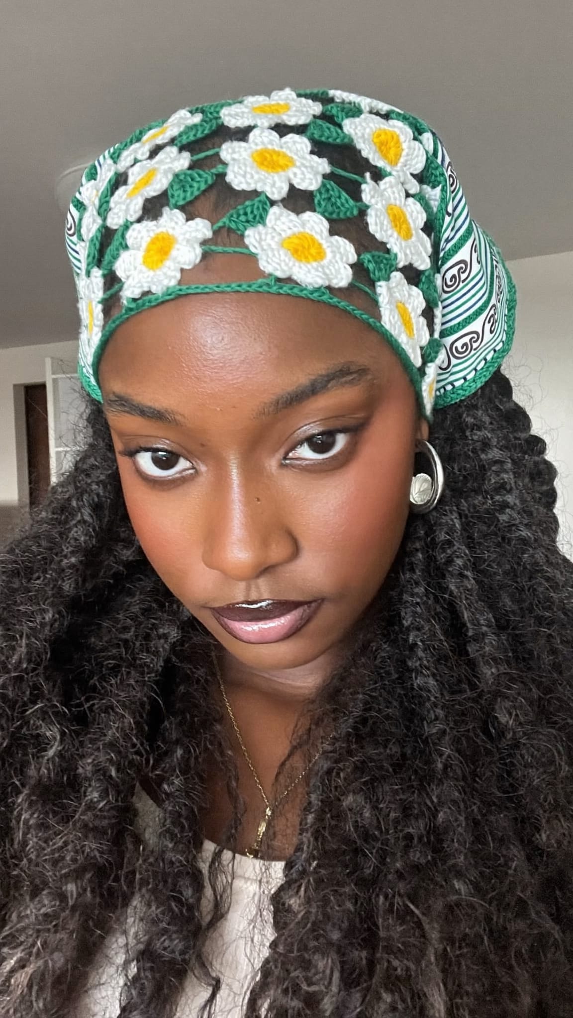 Black woman with voluminous crochet braids wearing a crochet daisy headband bandana across the front