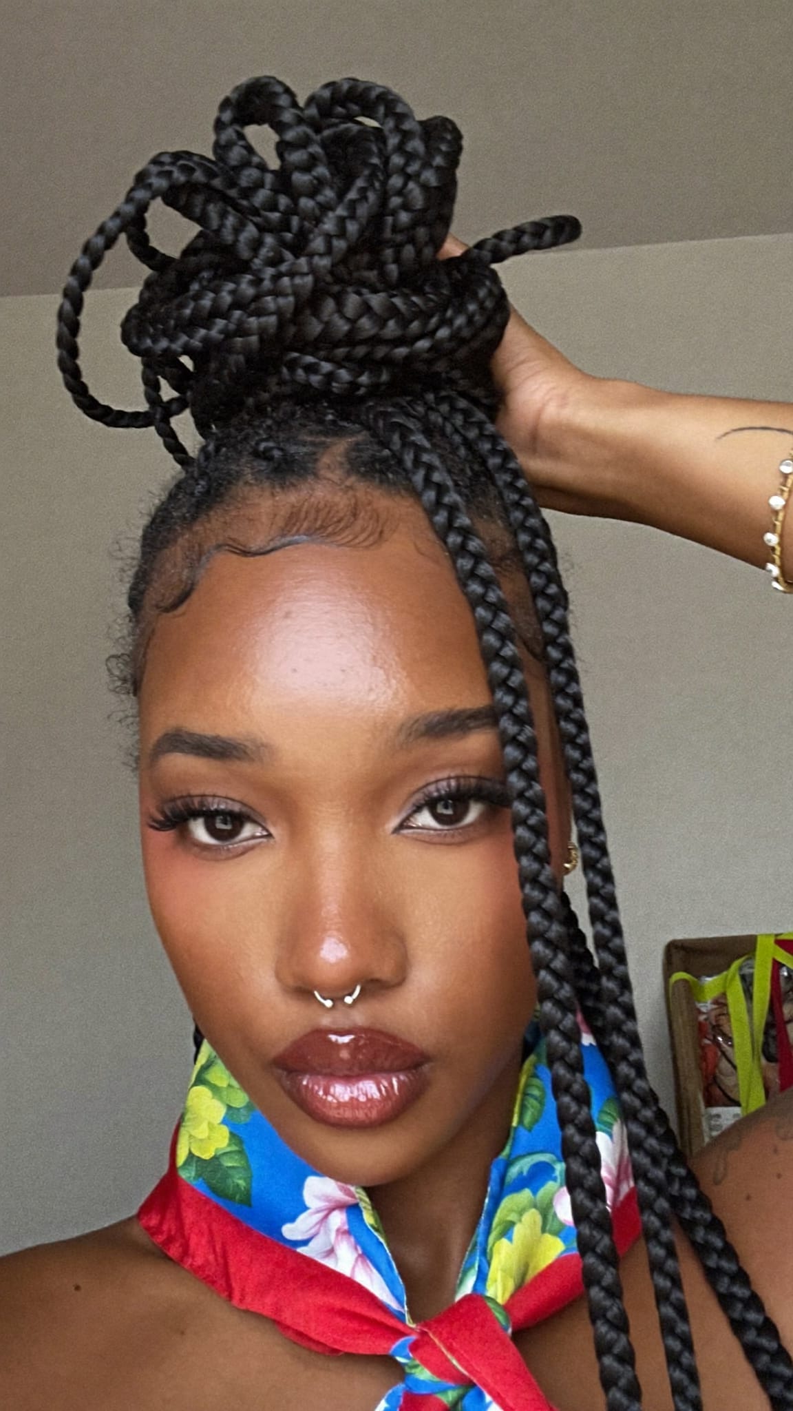 Black woman with box braids half pulled up in a high puff wearing a floral square bandana tied in a knot at the base