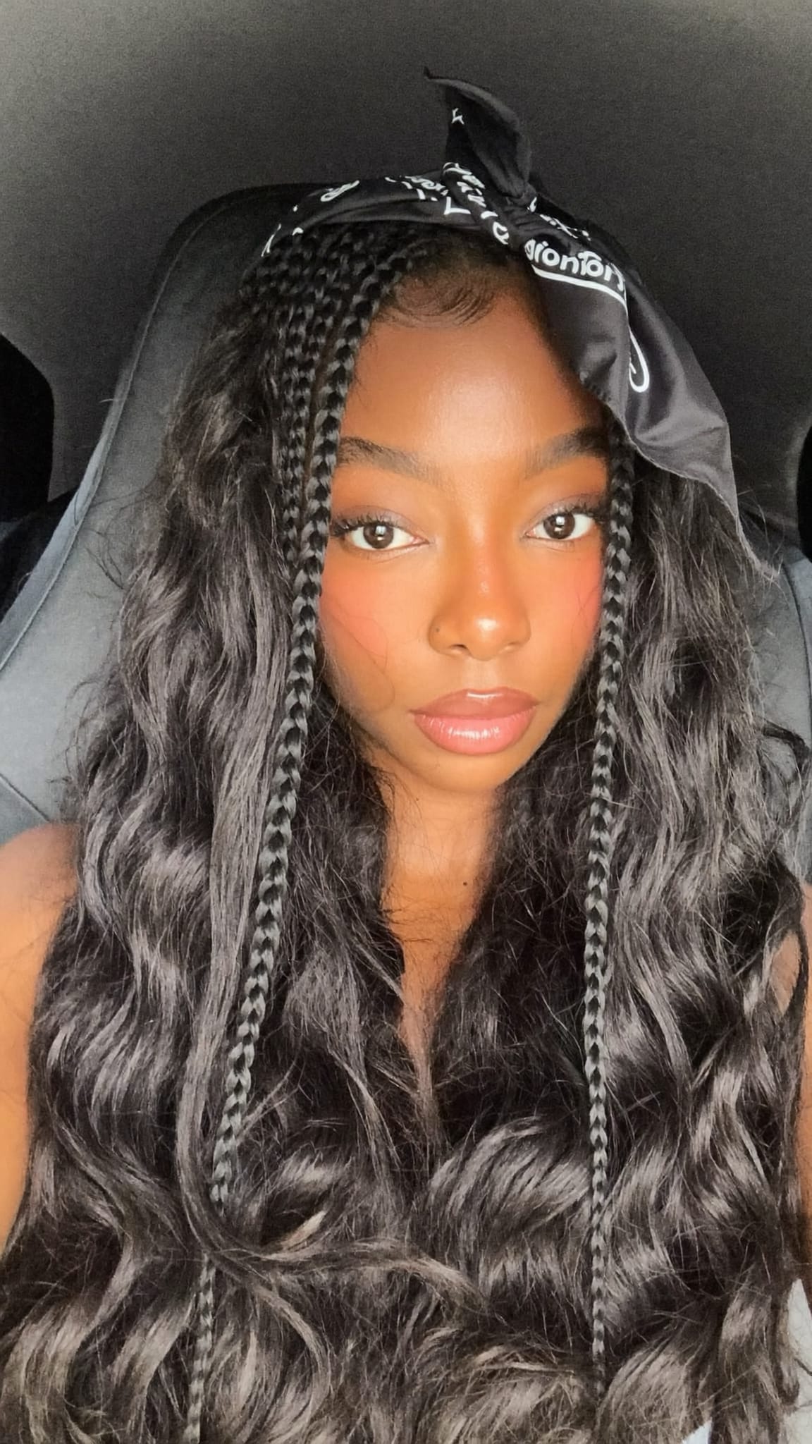 Black woman with long single plaits wearing a satin bandana tied around the gathered tails at the end