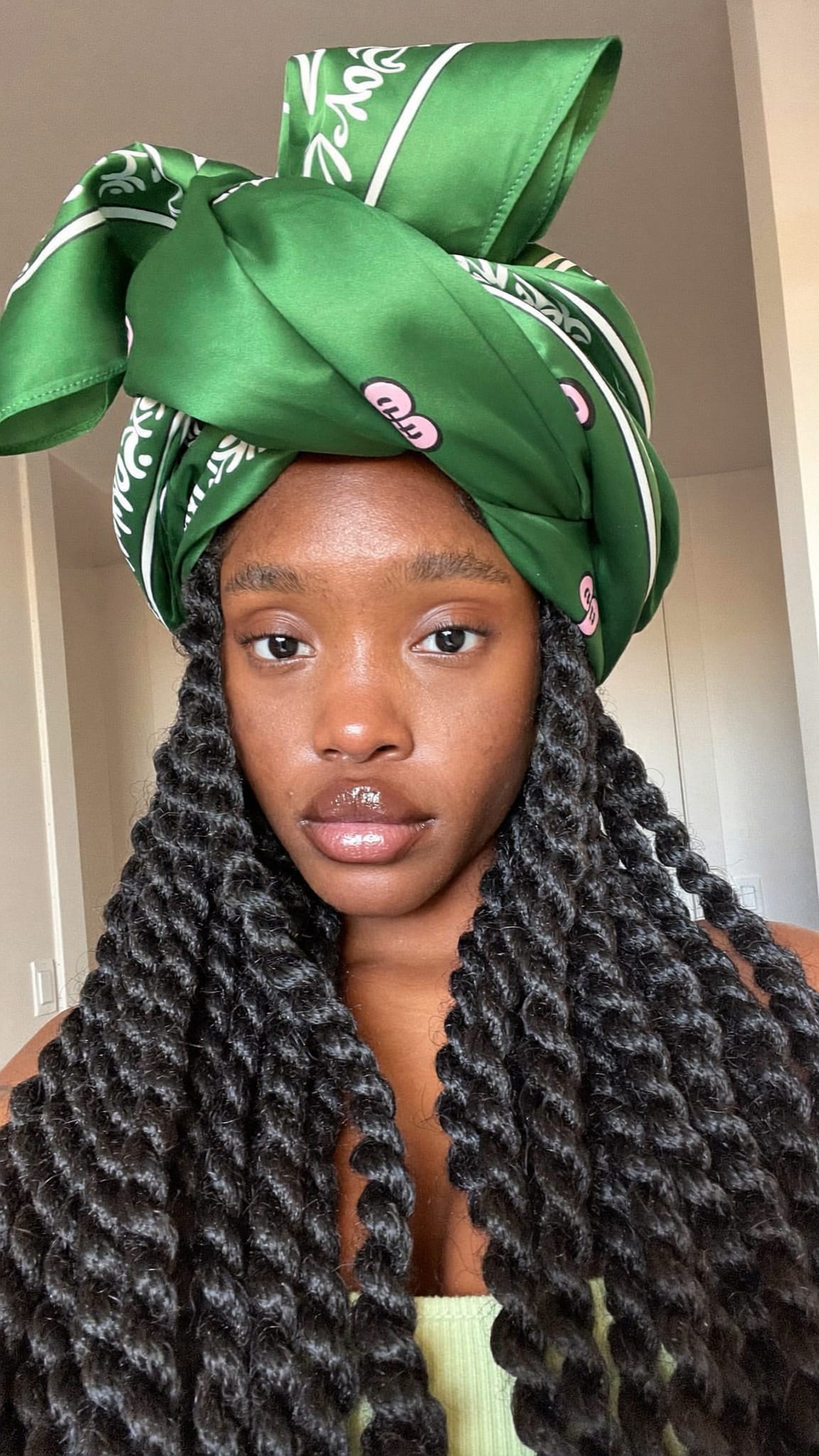 Black woman with long Senegalese twists wearing a large satin green silk-like bandana wrapped around the top of her head