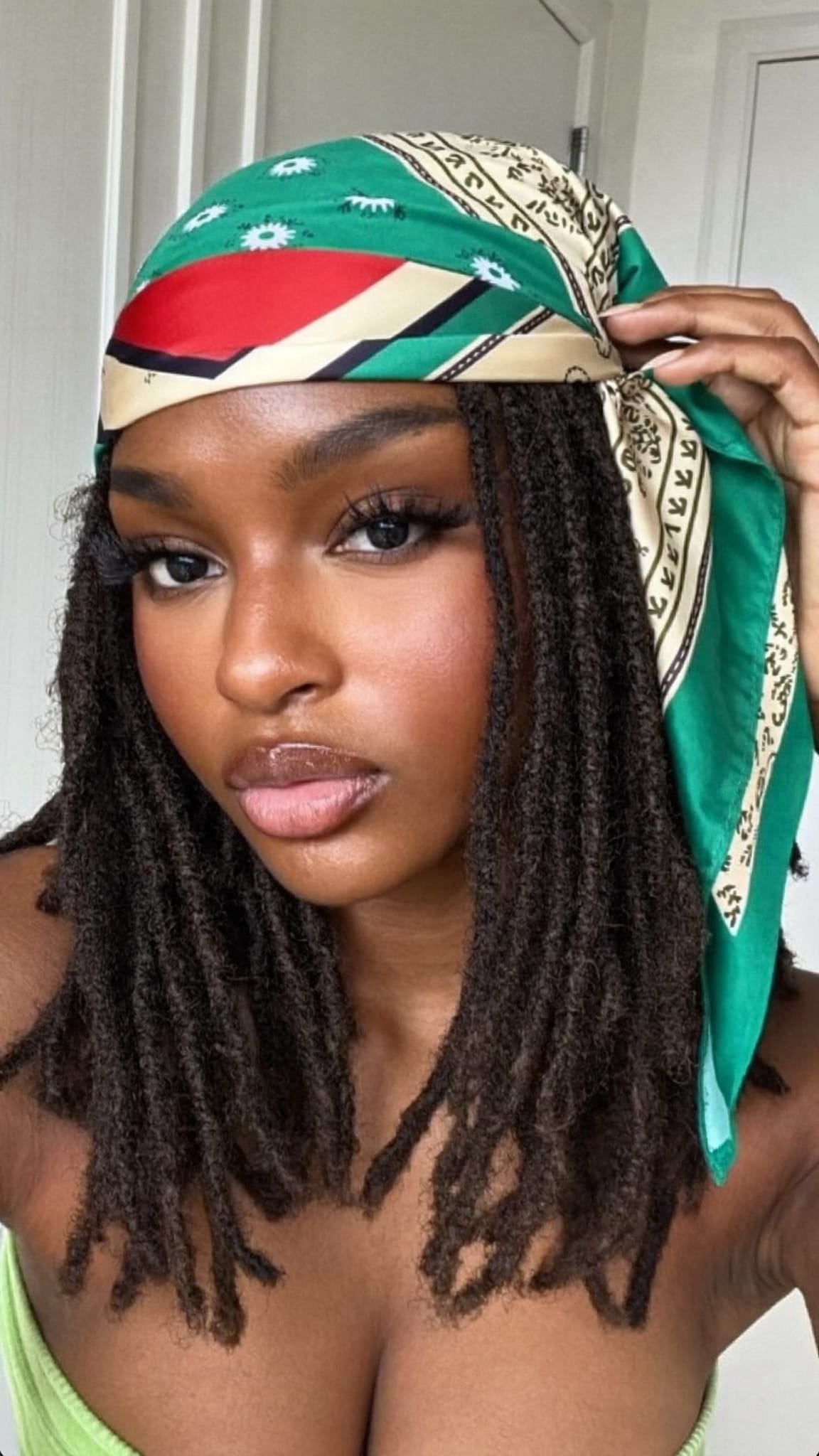 Black woman with medium faux locs wearing a vintage satin bandana tied around the head at the hairline