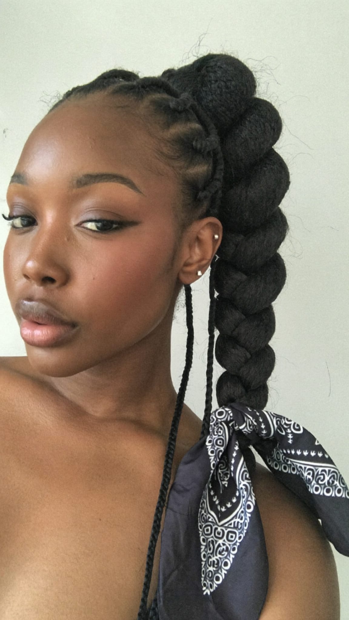Black woman with knotless braids pulled into a high sleek ponytail wearing a silky satin bandana tied at the base