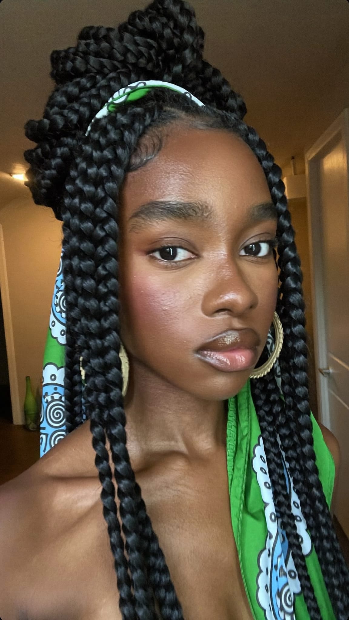 Black woman with thick goddess braids styled in an updo with a silk-like satin bandana woven through the braids