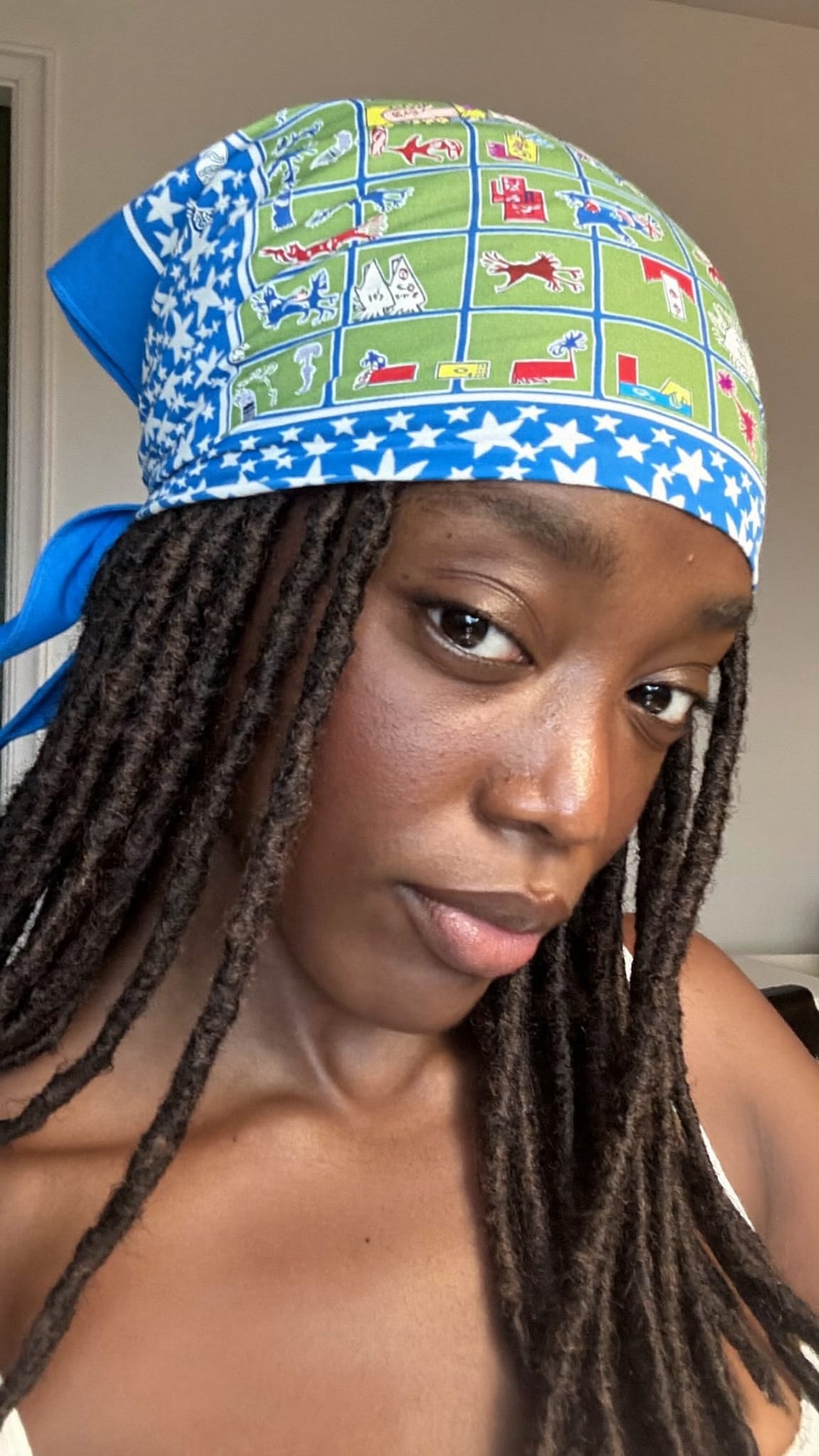 Black woman with medium-length locs wearing a large square island print bandana tied at the crown
