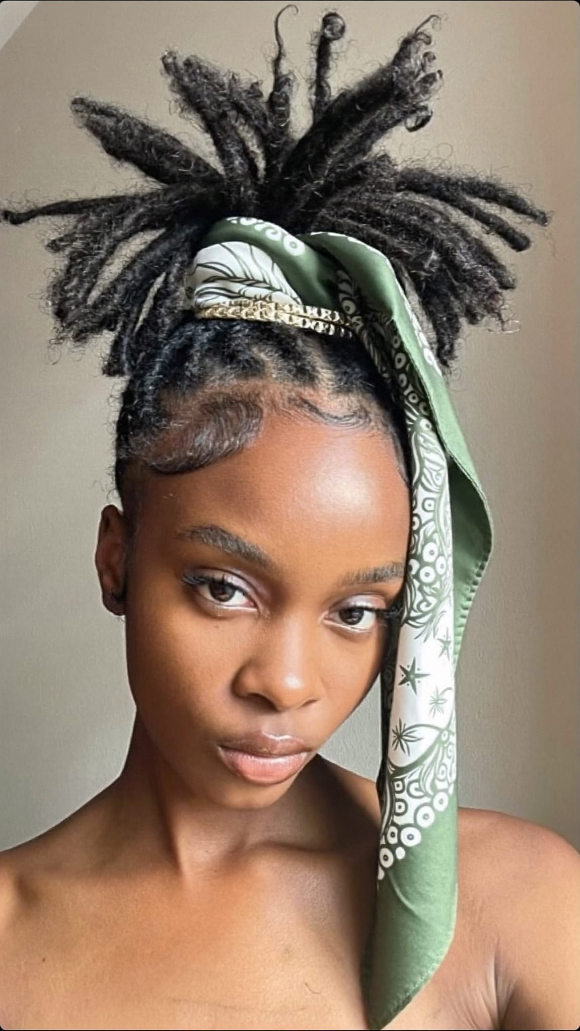 Black woman with locs styled in a high updo bun wearing a satin silk-like bandana as a crown accent