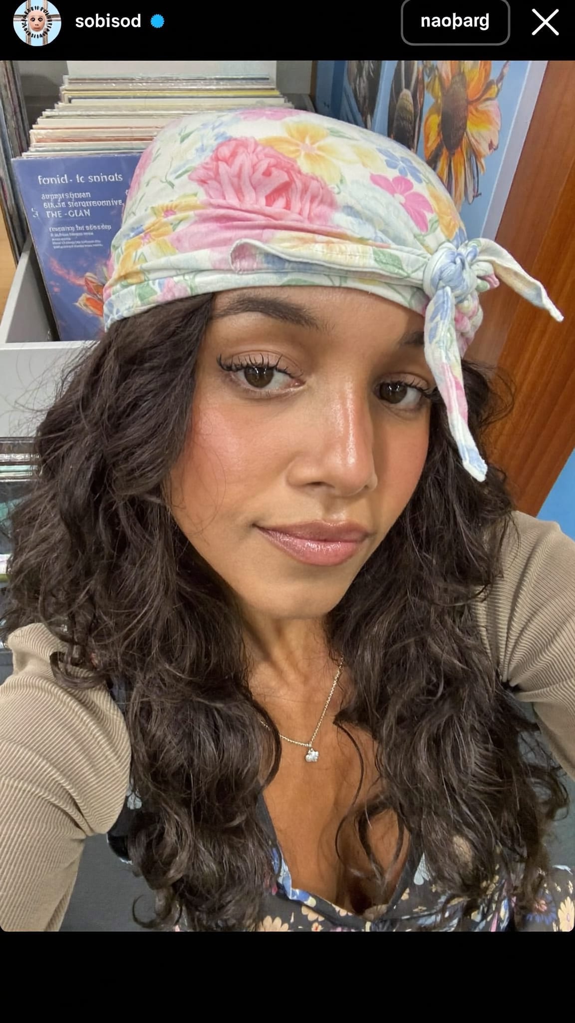 Mixed-race woman with wavy dark hair wearing a soft floral cotton bandana tied in a loose crown knot on top of her head, 90s indie alternative girl aesthetic, wearing a floral dress over a long-sleeve shirt, record store setting