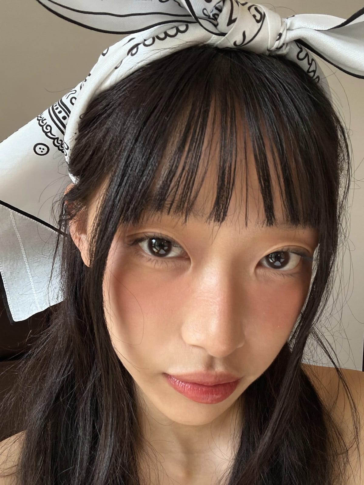Woman with curtain bangs wearing a silk square bandana folded as a headband behind her fringe