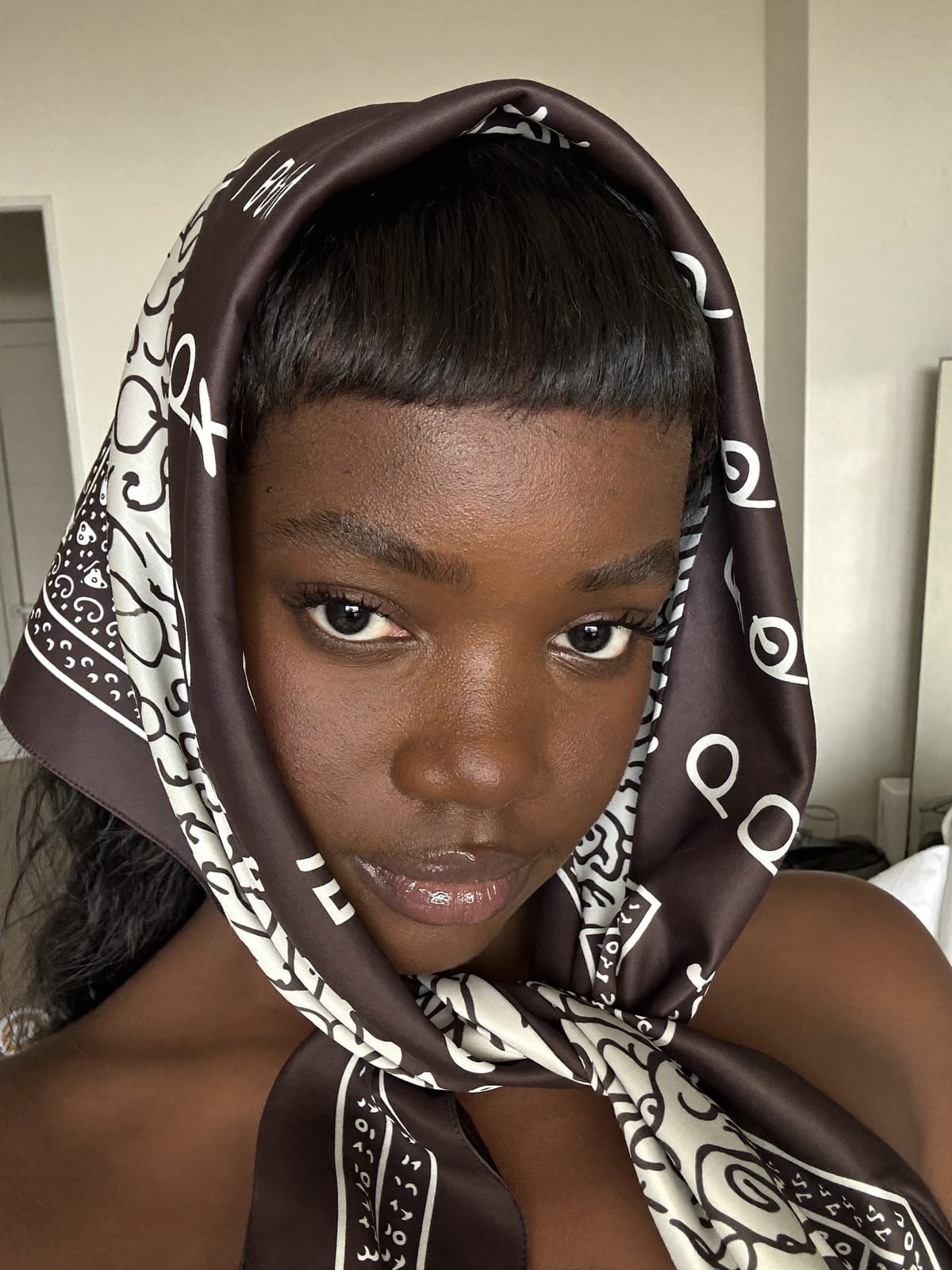Black woman with very short micro bangs wearing a large bold satin bandana pushed far back on her head