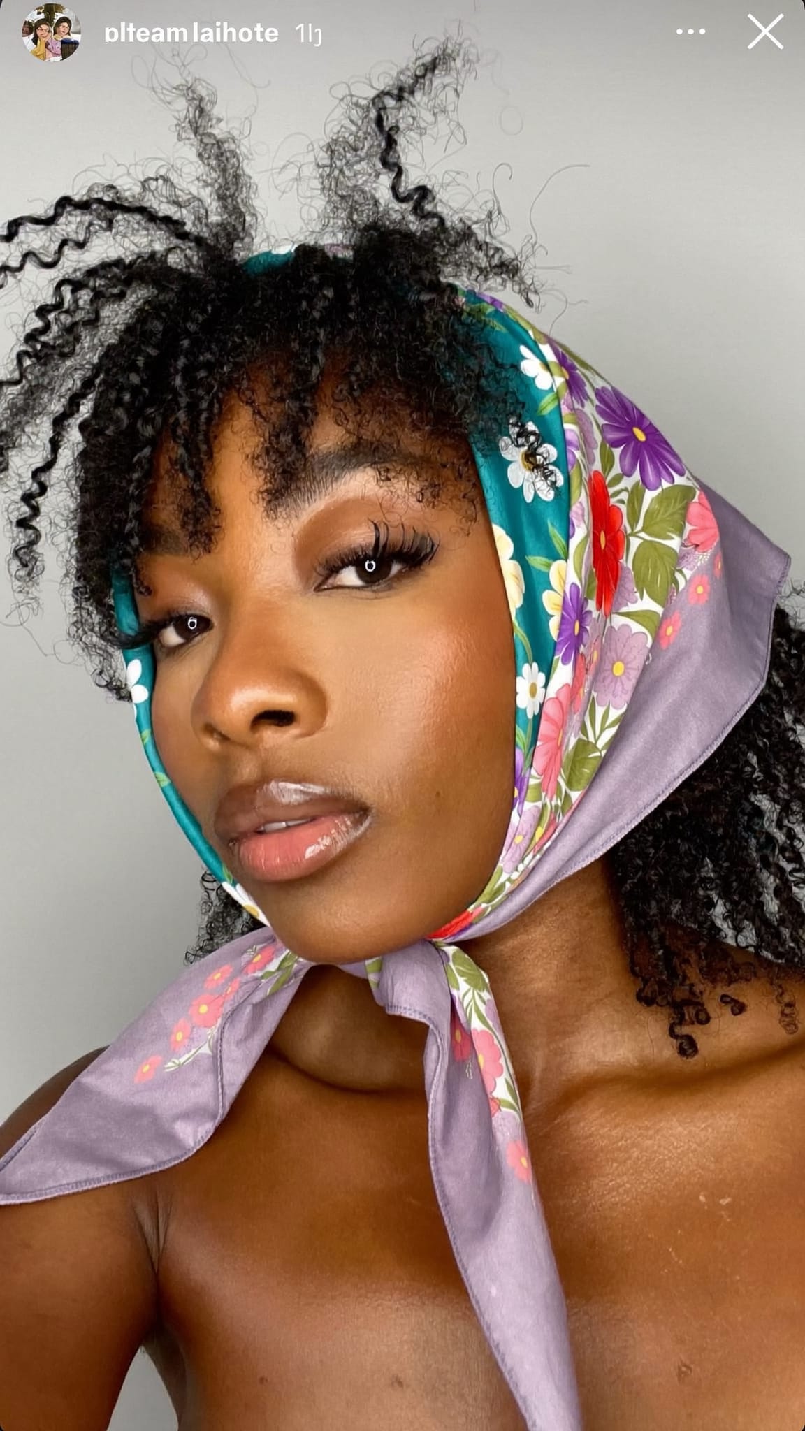 Black woman with natural curly bangs wearing a floral triangle bandana wrapped over the ears and tied at the nape