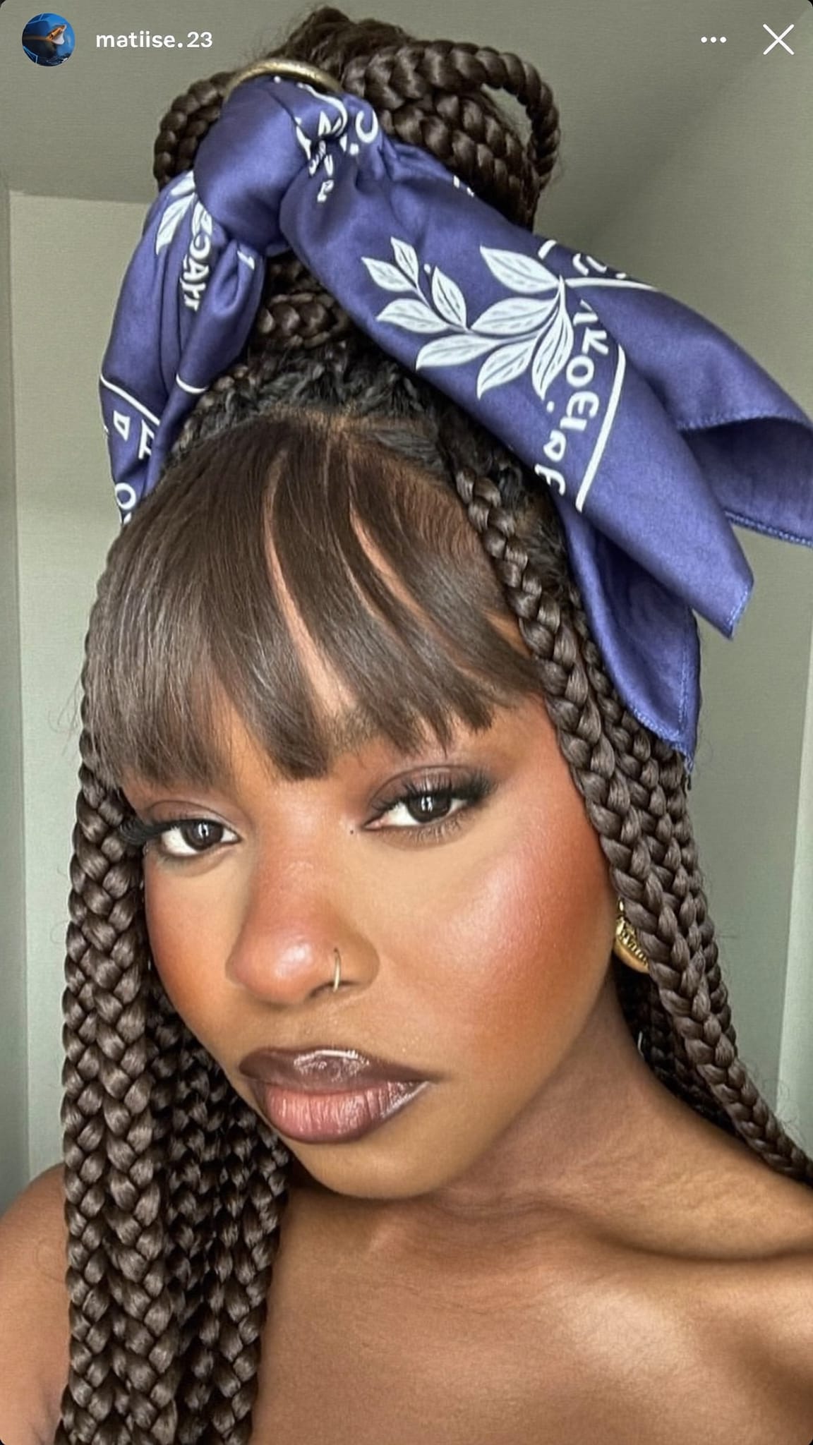 Black woman with box braids and straight-cut bang fringe wearing a large satin bandana wrapped as a crown over her braids