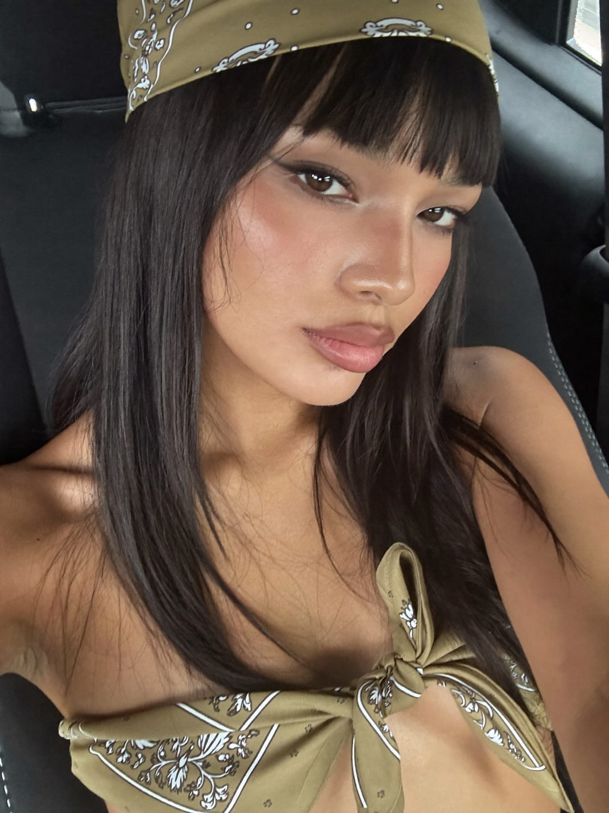 South Asian woman with thick blunt fringe bangs wearing a khaki floral triangle bandana tied at the nape