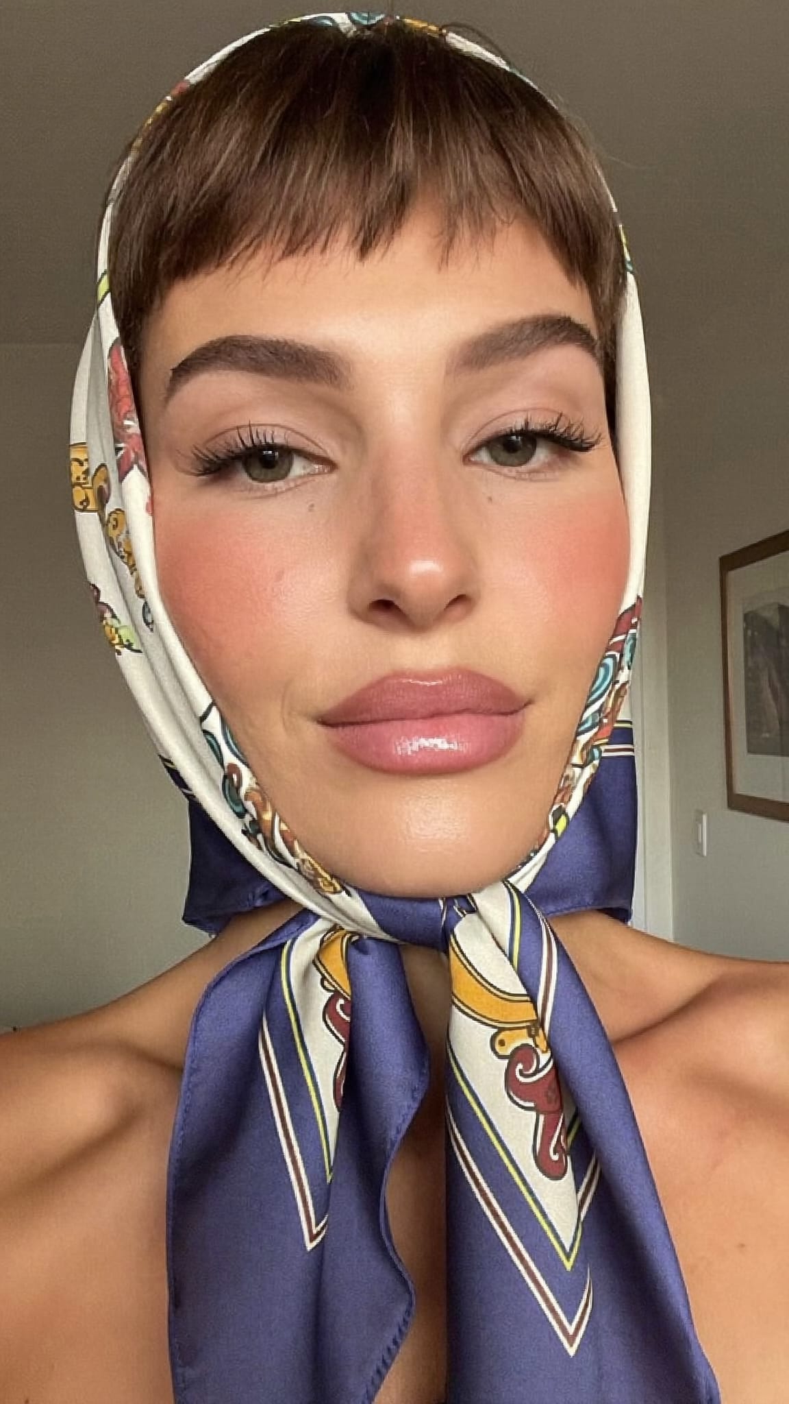 White woman with short blunt forehead fringe wearing a long skinny silk scarf twisted and wrapped around her head