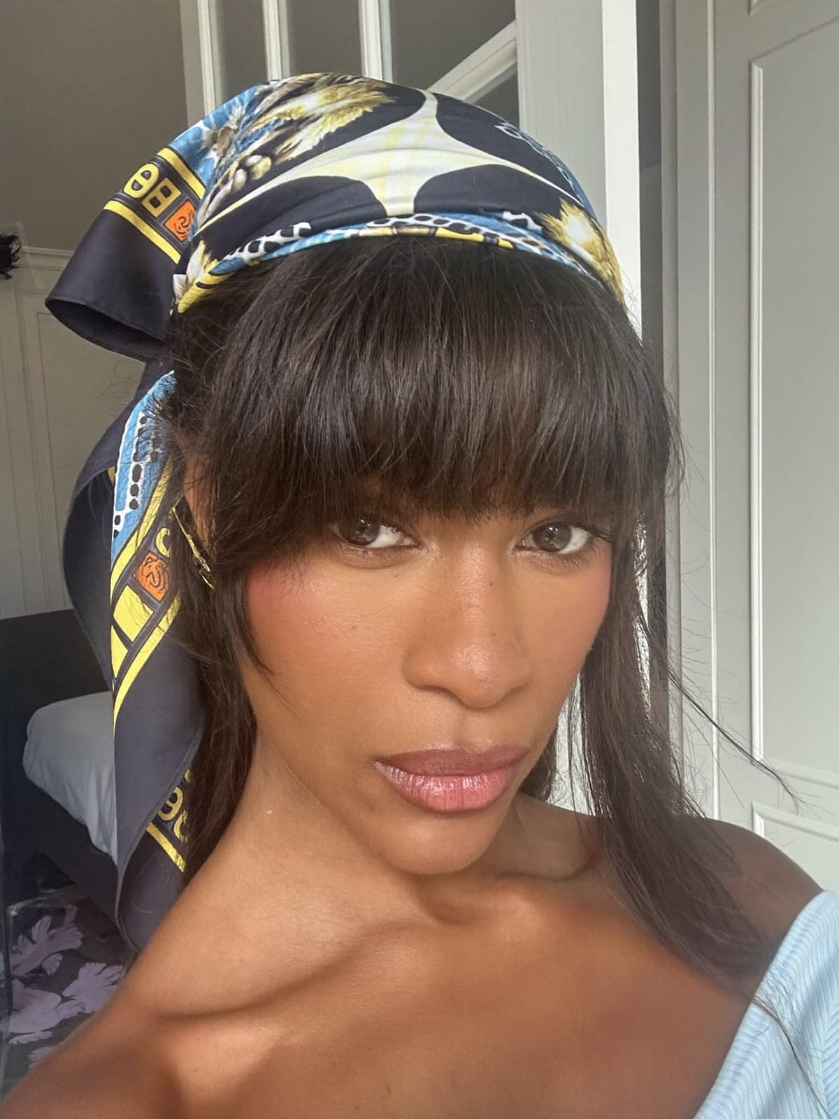 French-looking woman with full dense French fringe bangs wearing a large silk satin headscarf tied at the back