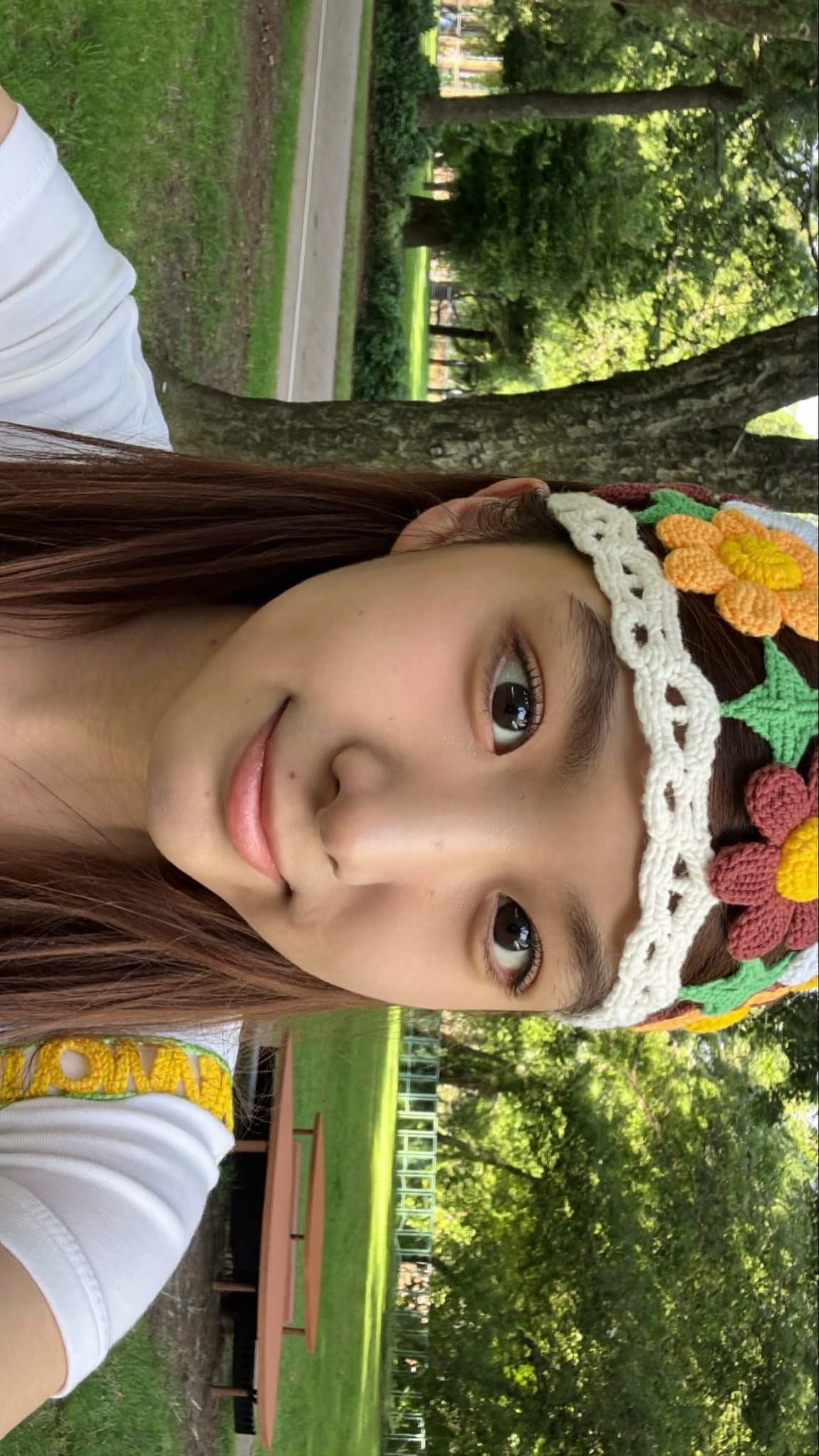Teen girl with straight hair wearing a colorful crochet daisy flower headband bandana, smiling at the park