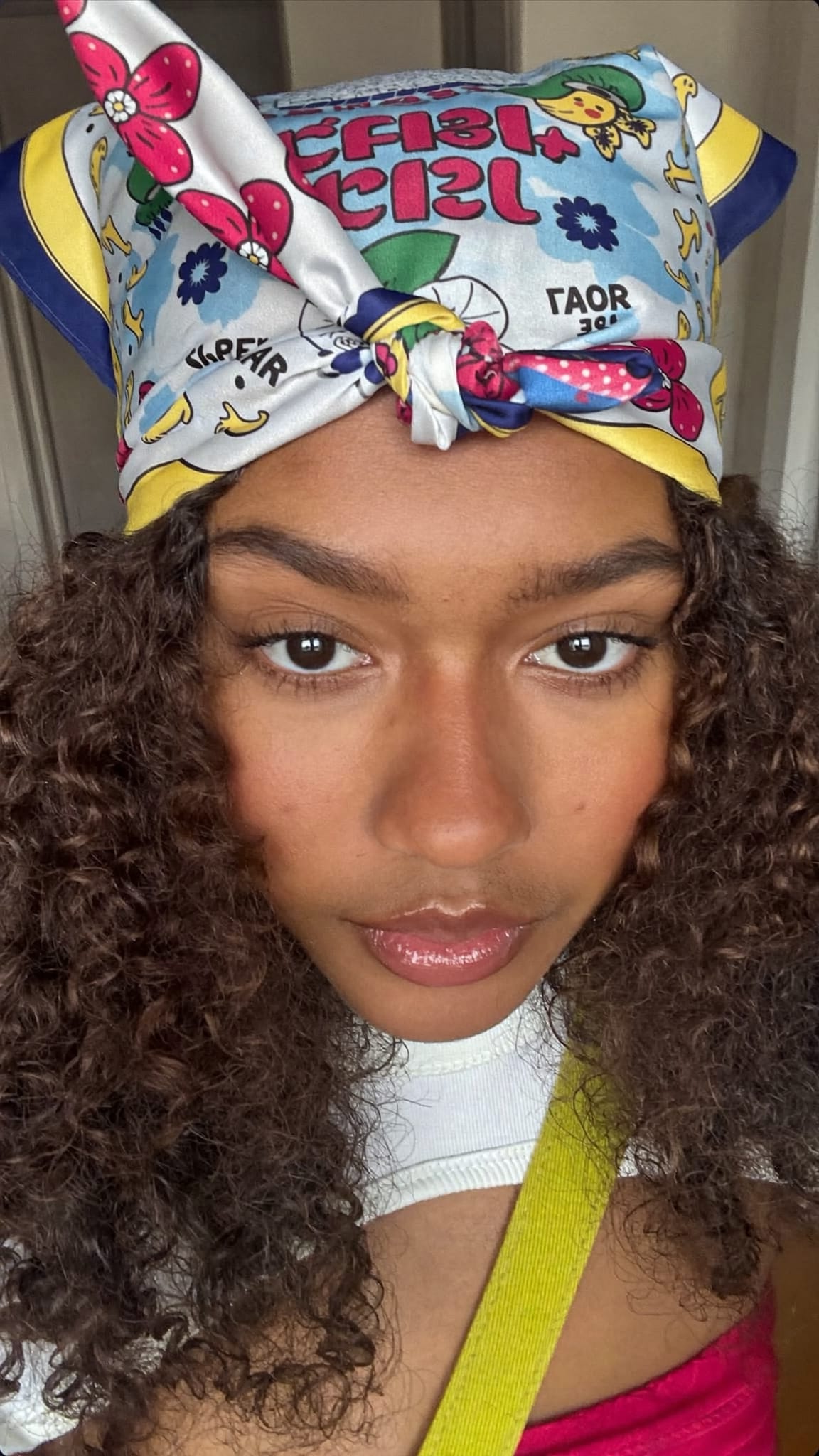 Teen girl with curly hair, a printed silk-feel square bandana tied at the forehead in a cute knotted bow