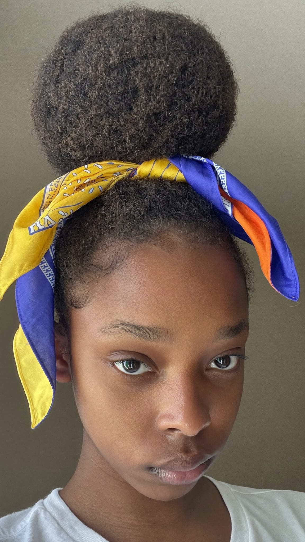 Young Black teen with a big poofy bun, a colorful satin bandana tied around the base with ends hanging loose