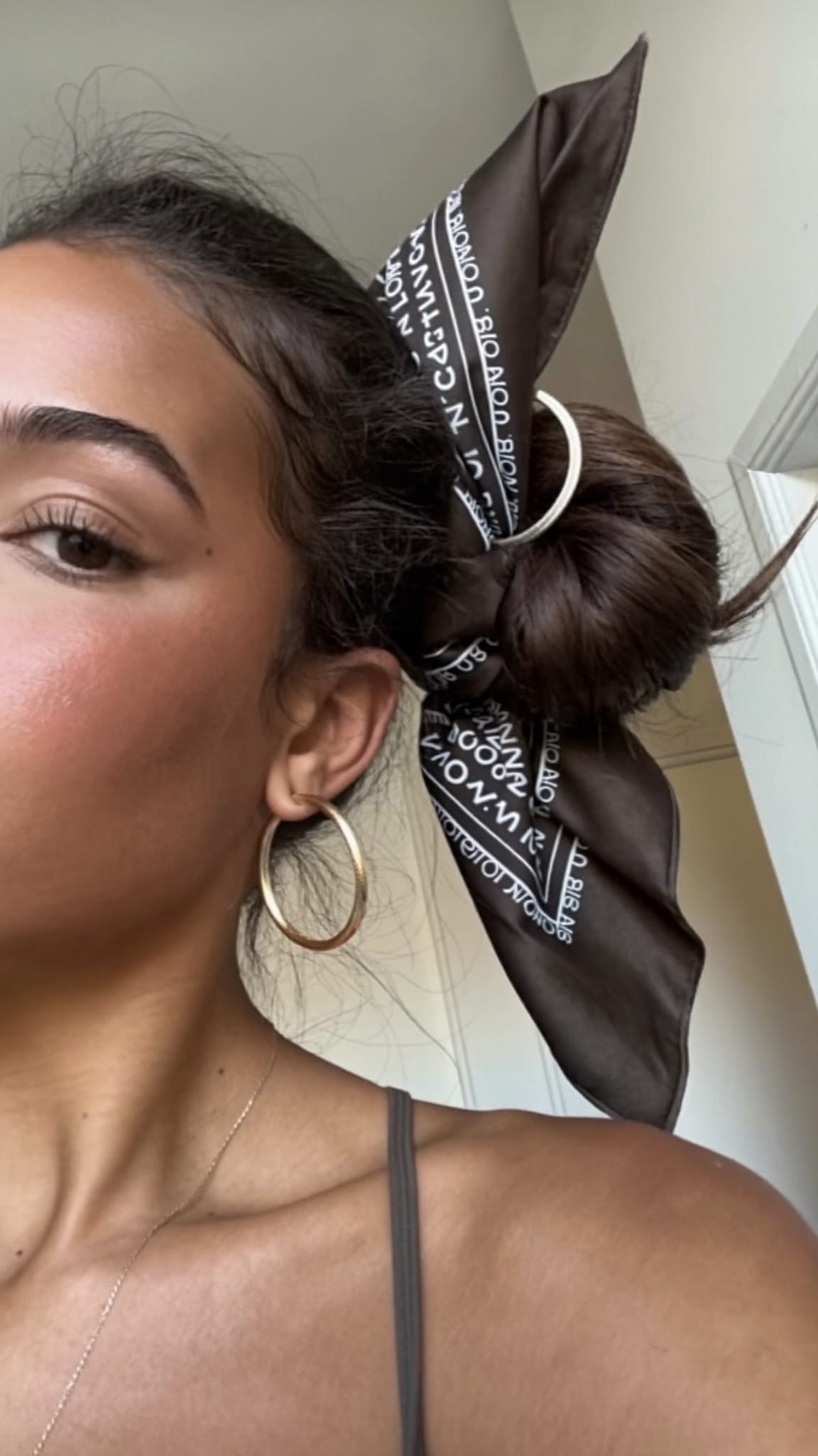 Latina woman with olive skin and a messy bun with a satin bandana tied around the bun as an anchor