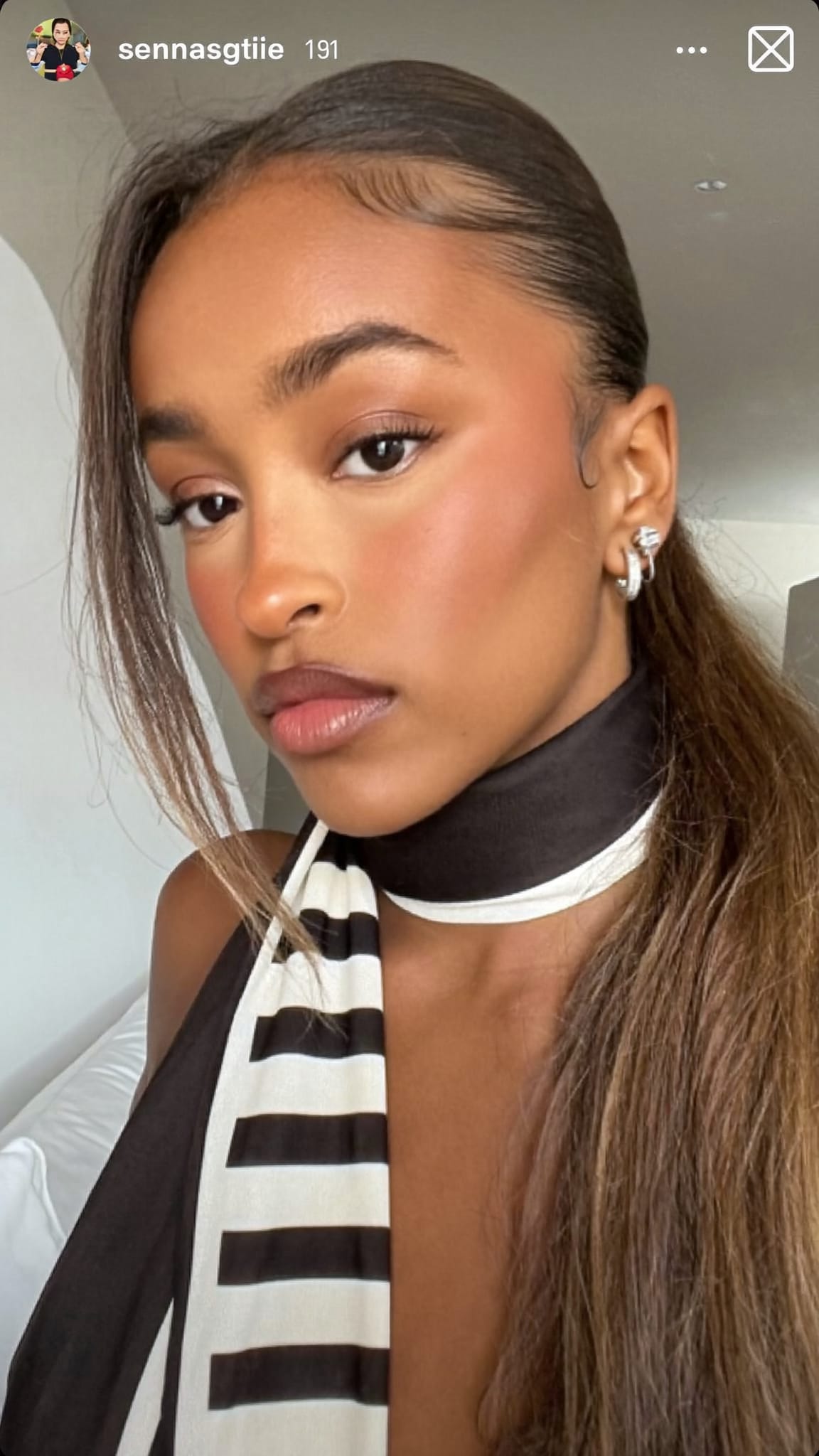 Woman with medium brown skin and long straight hair with a long skinny scarf wrapped through and around a low ponytail