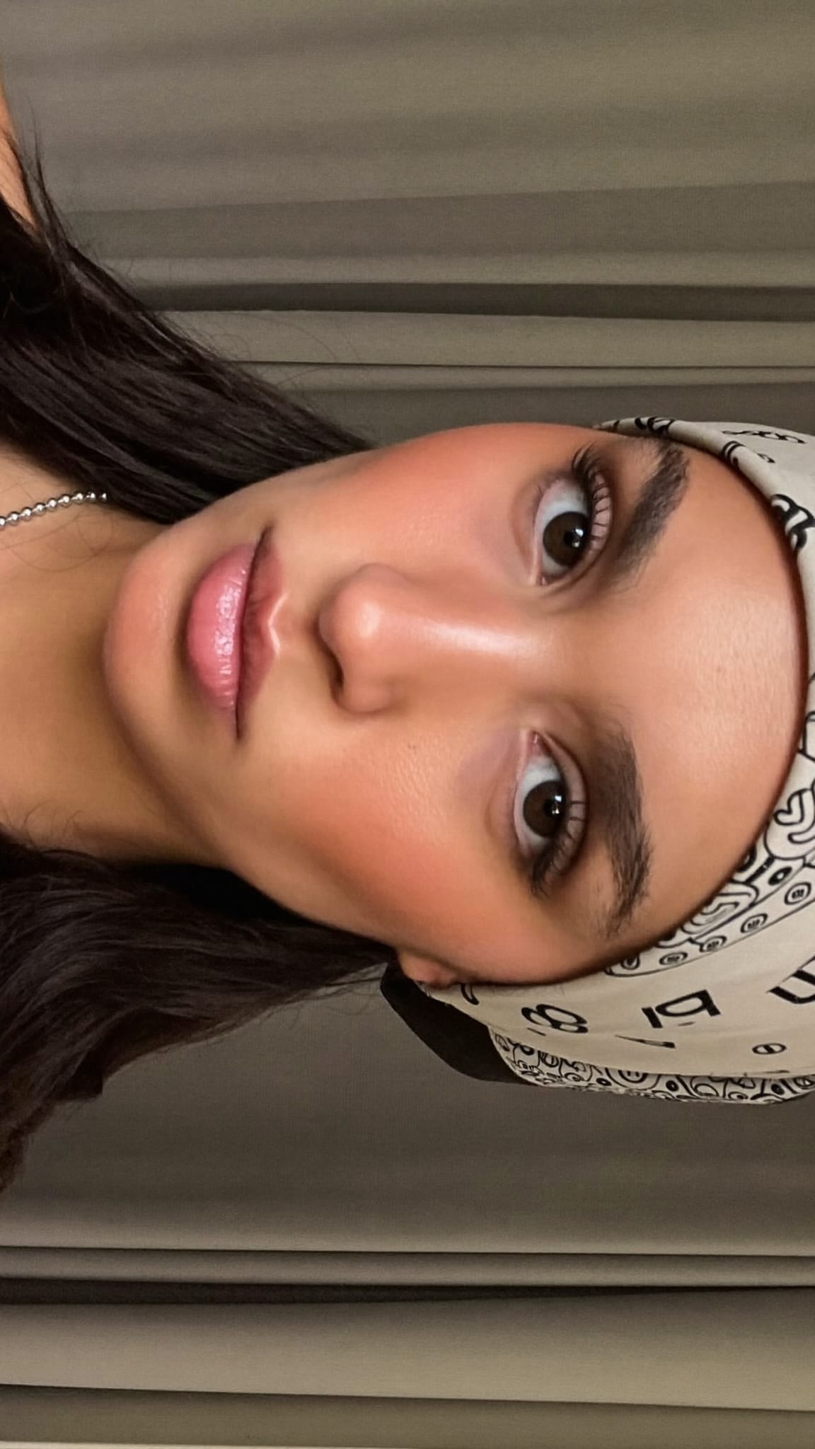 Woman with olive skin and long dark hair slicked back low with a printed satin bandana wrapped around the perimeter