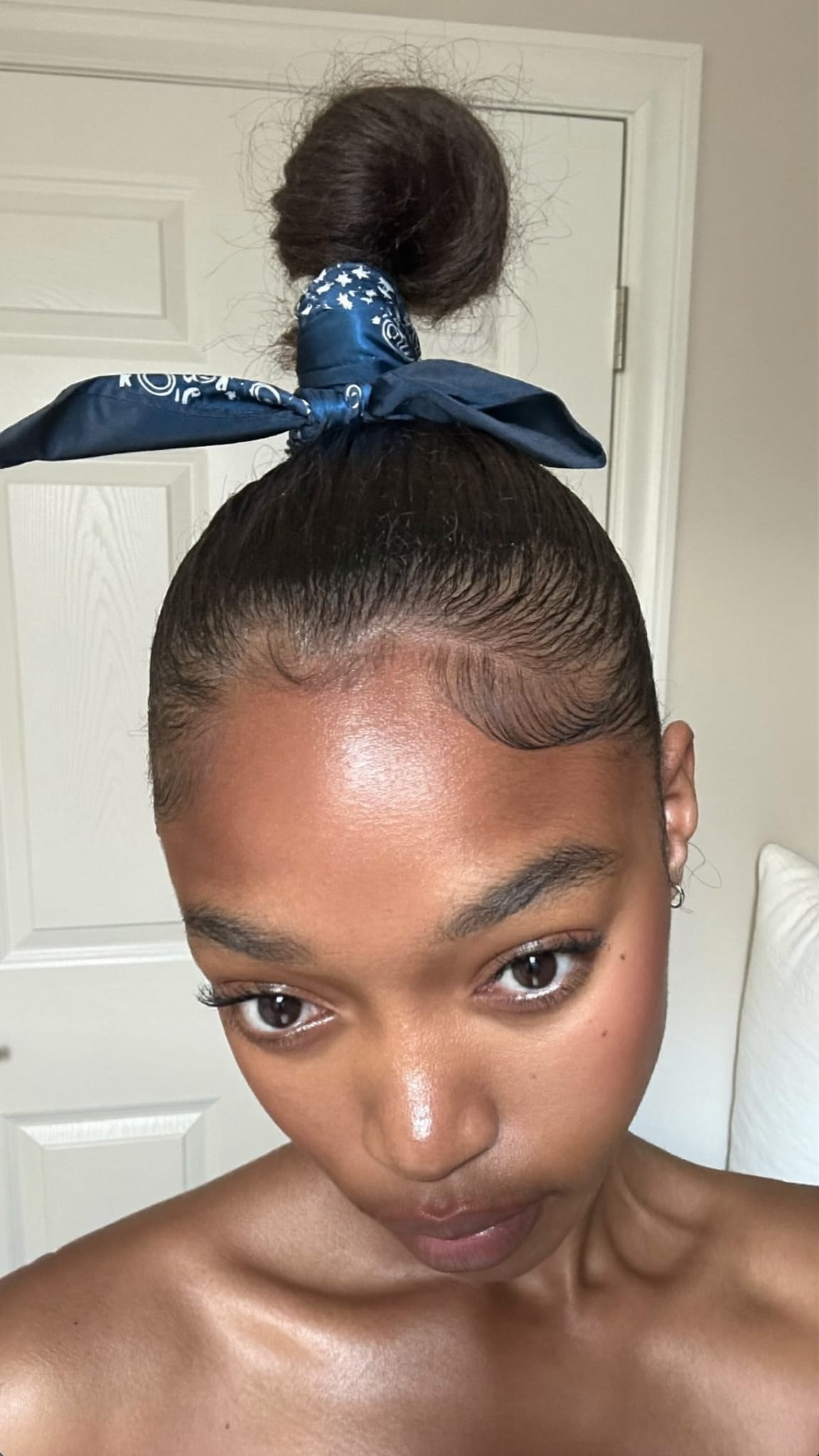 Woman with medium-brown skin and hair in a high top knot bun with a silk bandana tied around the bun in a finishing knot