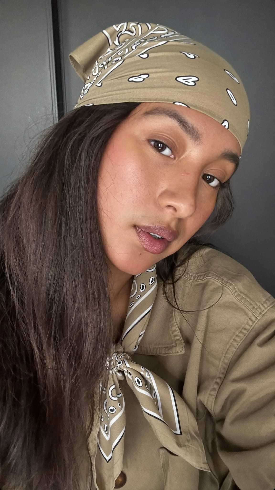 South Asian woman with long dark hair wearing a khaki triangle bandana knotted at the nape