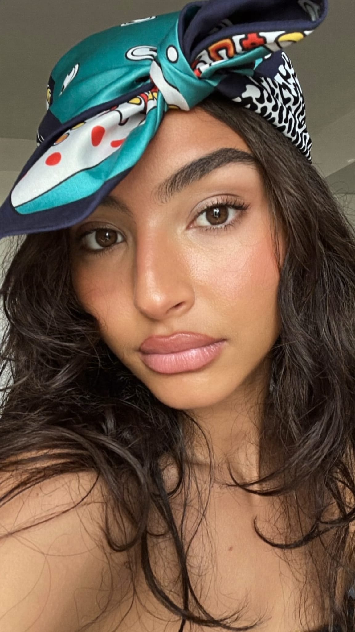 Latina woman with wavy hair wearing a silk satin bandana knotted high at the crown