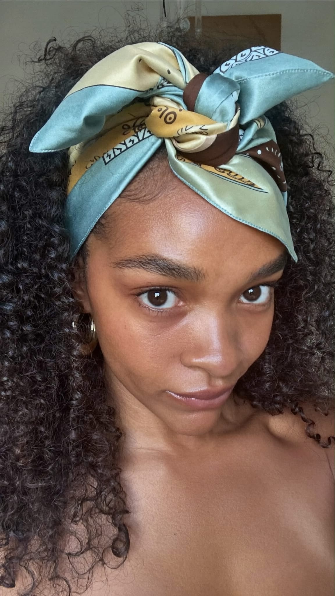 Mixed-race woman with curly hair wearing a twisted satin bandana headband with the twist sitting at the top