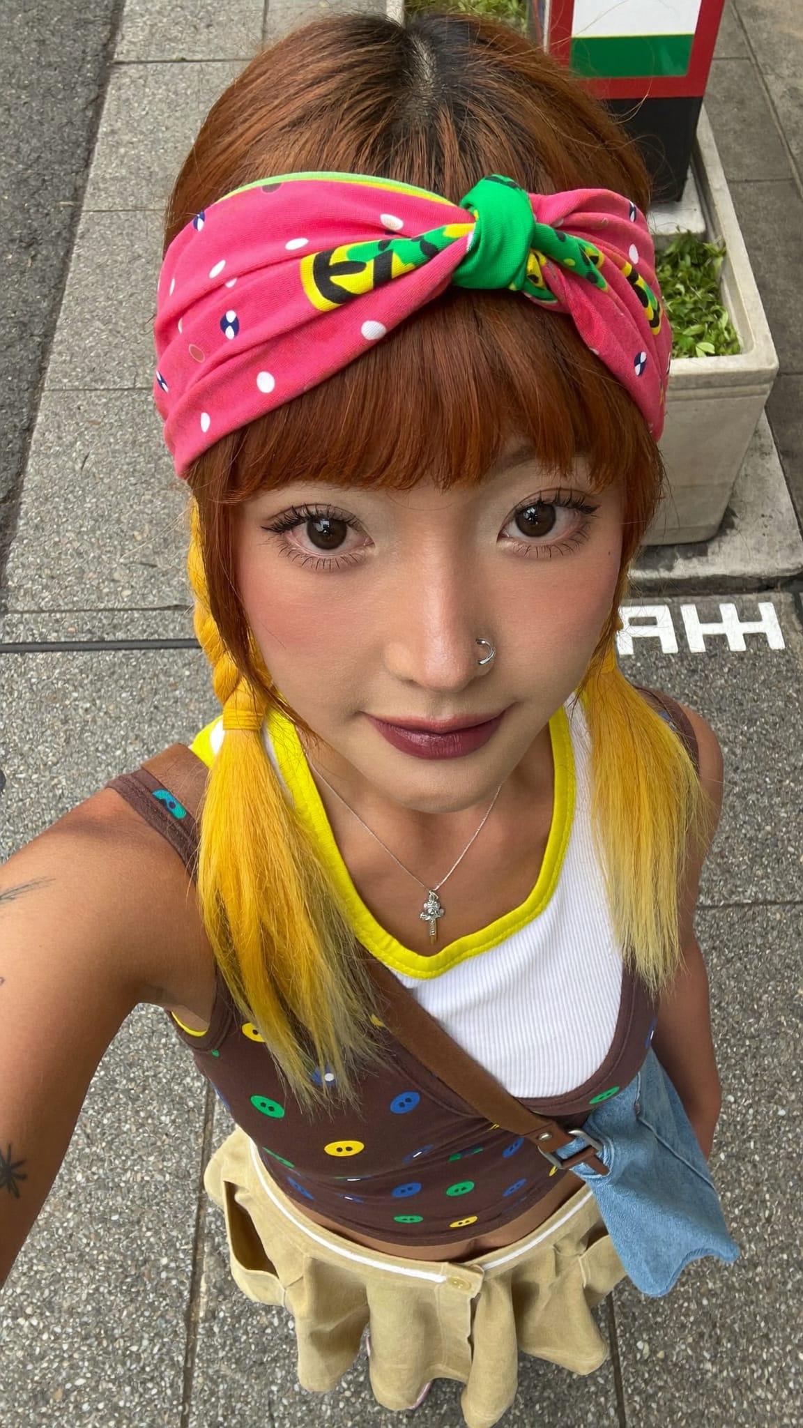 East Asian woman in her 20s with colorful pigtails and a bright boho elastic bandana headband with a central knot, wearing a layered kawaii outfit in a Japanese streetwear setting