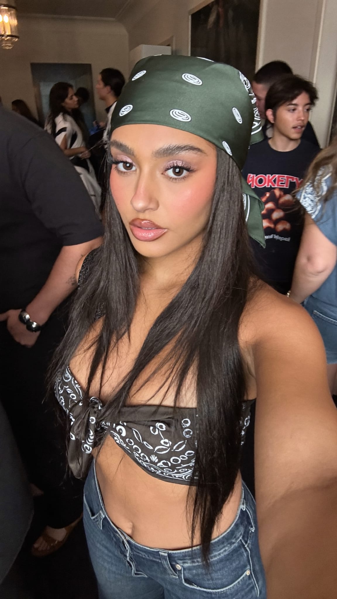 Mixed-race woman in her 20s with long straight hair and a silk satin bandana tied as a narrow headband, wearing a crop top and ultra-low-rise jeans at a Y2K-era house party