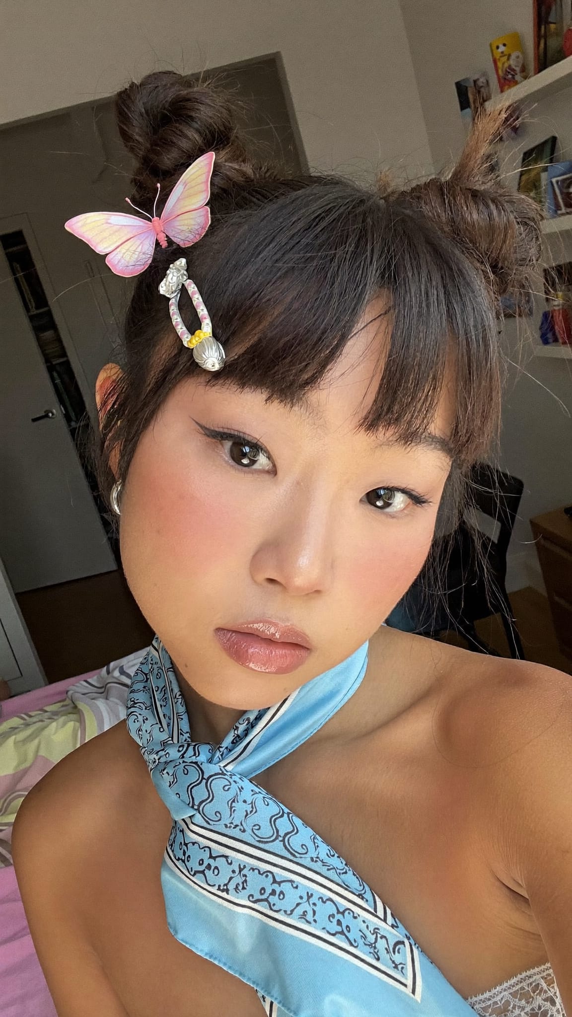 East Asian woman in her 20s with dual space buns and a silk square bandana headband, wearing a butterfly-clip-accented outfit in a Y2K-era bedroom setting